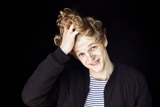 Portrait of smiling young man with hand in hair against black background