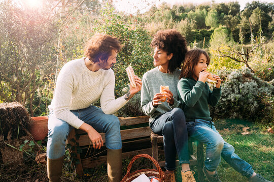 Happy family siting in garden, taking a break, eating sandwiches