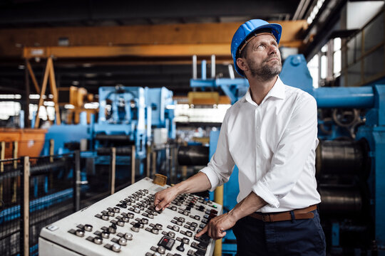 Male entrepreneur operating control panel looking up while standing at industry