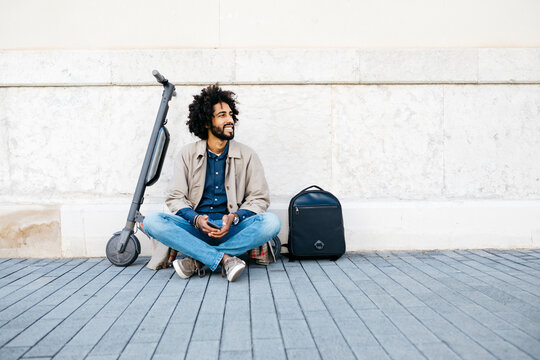 Smiling young man with cell phone sitting on his E-Scooter looking at distance