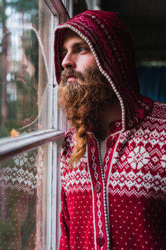 Portrait of pensive man with beard wearing hooded jacket looking out of window