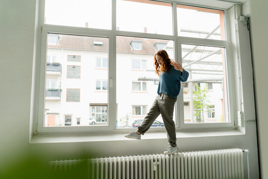 Redheaded woman balancing on heater in a loft