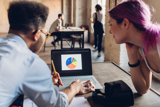 Two creative business people hanalyzing chart on laptop screen in loft office