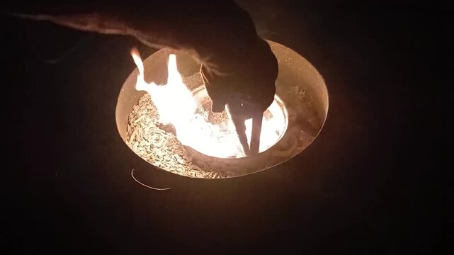 Stock video: heating in a barrel with a small pot inside and melting plastic, hand holding a metal tip turns the plastic over, flame becomes larger.