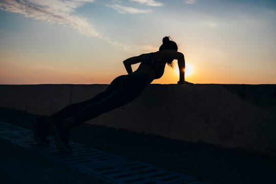 Full length of silhouette female athlete doing push-ups at promenade during sunrise