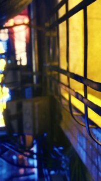 A narrow urban alley shows bright lights reflecting off the walls. Cables hang above, and the vibrant colors add energy to the setting. People may pass through on their way somewhere else.