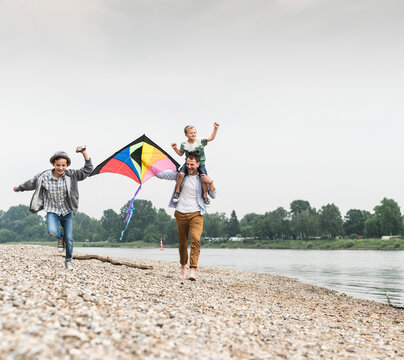 Happy father with two sons flying kite at the riverside