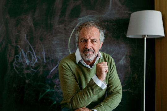 Mature man sitting against blackboard at home
