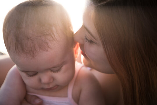 Primo piano di una madre che bacia teneramente la testa della sua bambina piccola al tramonto