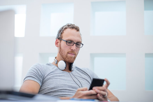 Young man with headphones around his neck reading text messages on his phone