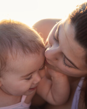 Primo piano di una madre che bacia teneramente la testa della sua bambina piccola al tramonto