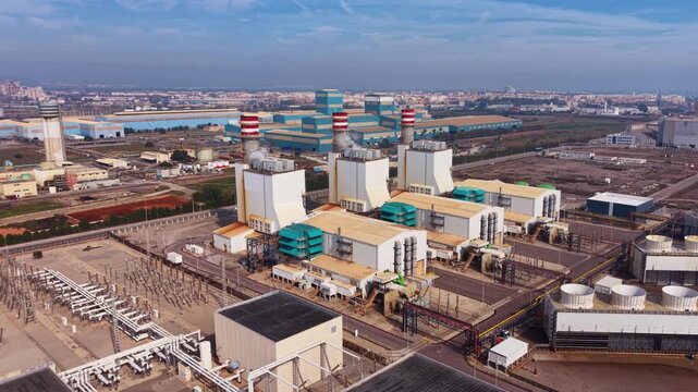 Aerial view of a combined cycle gas power plant with gas turbines, heat recovery steam generators, exhaust stacks and high-voltage switchyard delivering electricity to the transmission grid