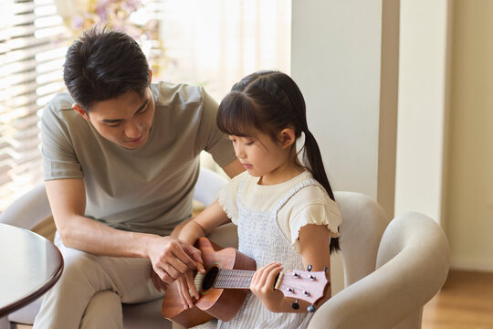 A girl following an online ukulele lesson, with her dad accompanying her