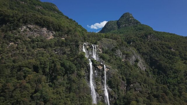 Drone flying towards spectacular Acquafraggia waterfalls cascading down a green mountain in Val Bregaglia, Italy. Aerial forward