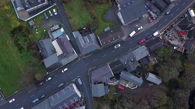 Top down aerial drone shot capturing the streets and rooftops of a small Irish town and the daily life below, moving vehicle and local businesses