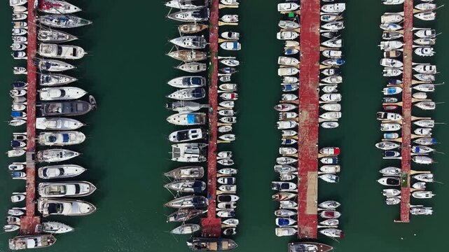 Boats are parked neatly in rows at a marina. The scene shows an overhead view with docks filled with different watercraft. This is a busy setting in a coastal area during clear weather.