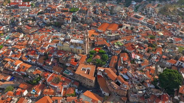 Aerial panoramic view of the Santa Prisca temple in Taxco with tiled roofs and slopes due to its construction between mountains, sunny day, Guerrero, Mexico