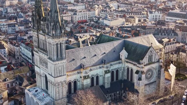 Drone pulls back from Saint-Maurice Cathedral at sunrise revealing historic city of Angers around the gothic monument.
