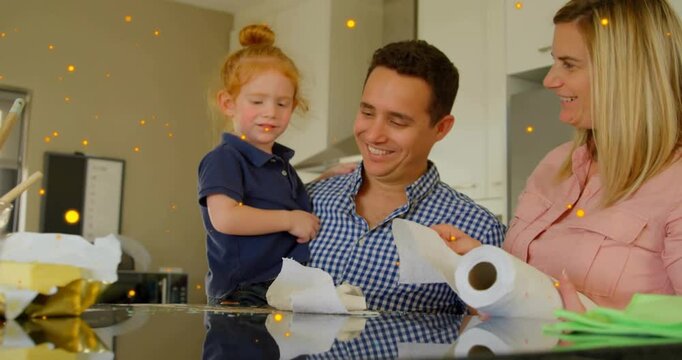 Father pointing to paper towel, child dabbing countertop, mother handing sheets, teaching homecare