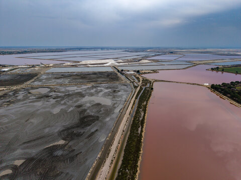Aerial view of striking contrasts between the dark, textured earth and the rosy hues of the salt marshes under a vast sky, Aigues-Mortes, Occitanie, France.