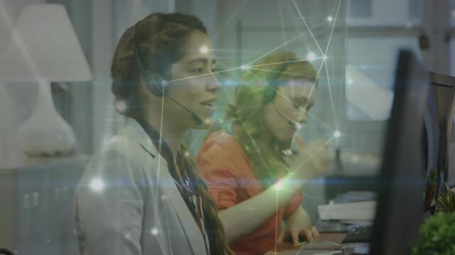 Camera panning two call agents one talking as other writing net overlay on screens handling calls
