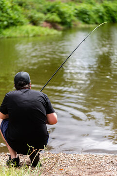 Man with fishing rod crouched by the edge of an inland river
