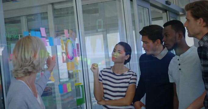 Presenter tapping notes on glass, team leaning, stepping, narrowing business plan with color wheel