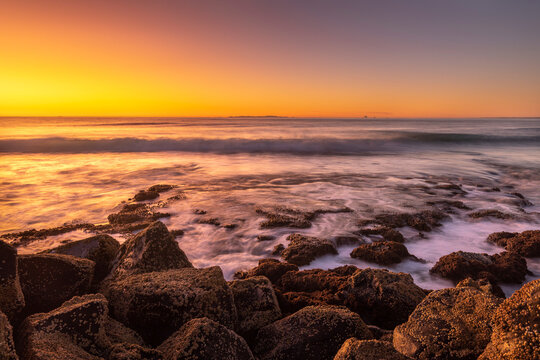 Barnacle covered rocks at sunset with waves crashing