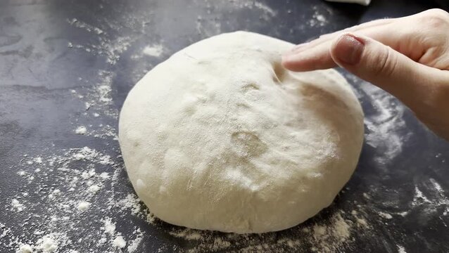 Close up of female hand checking the yeast dough if its ready on floured kitchen table 