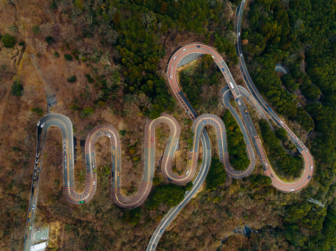 Aerial view of a winding road snaking through the terrain, cutting through the dense forest, Nikko, Tochigi, Japan.