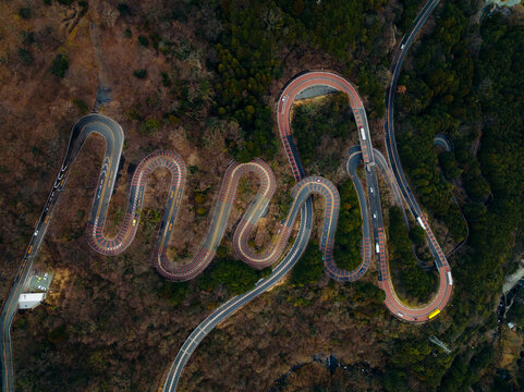 Aerial view of a winding, serpentine road cutting through the forested hills, its curves accentuated by the changing light and shadows, Nikko, Tochigi, Japan.