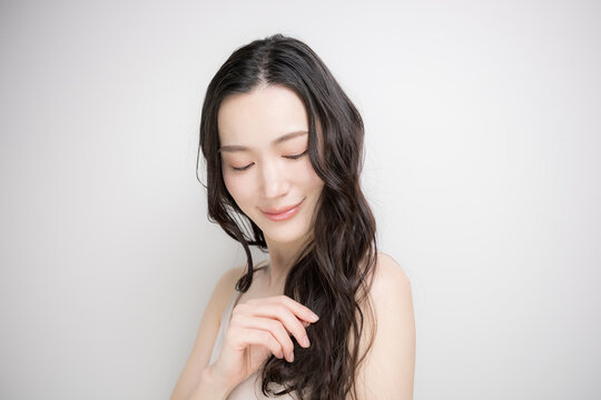 白背景に綺麗な黒髪をなびかせるロングヘアでパーマの女性　ヘアケアやトリートメントイメージ目を閉じる