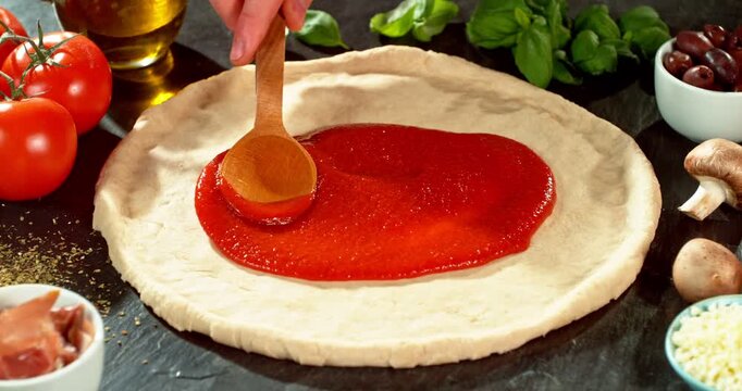 Super slow motion close-up of spreading tomato sauce on fresh pizza dough. Wooden spoon moves gently across the surface, highlighting texture, freshness and authentic Italian pizza preparation.