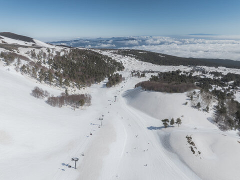 Aerial view of snow-covered slopes meeting stark tree lines, a winter wonderland contrasting with distant cloudscapes, Piano Provenzana, Sicilia, Italy.