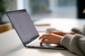 Fototapeta premium Blurred Person Typing on Laptop in Modern Office, Close-up of Hands and Keyboard
