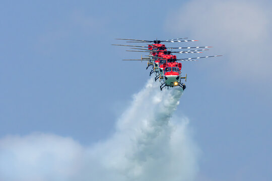 Aerial view of a dynamic acrobatic display of four red and white helicopters soaring through the sky, leaving a trail of white smoke, Singapore Air Show 2026, Singapore.