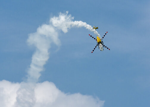 Aerial view of a helicopter soaring through the sky over the Changi Exhibition Centre, leaving a trail of white smoke against the blue sky, Singapore Air Show 2026, Singapore.