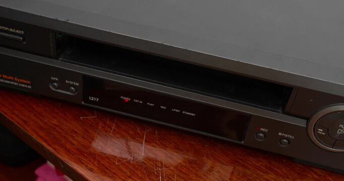 VHS cassette tape slides out of VCR during eject process. Retro media device and analog home entertainment technology