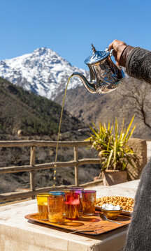 Moroccan Tea prepared in sunlight with Atlas mountains with snow in background, vertical.