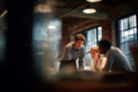 Blurred Diverse team collaborating on laptop in modern office space