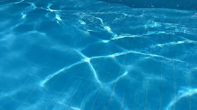 Clear blue swimming pool water with gentle ripples and reflections, showcasing the movement of light across the surface and the tiled bottom in a sunny outdoor setting