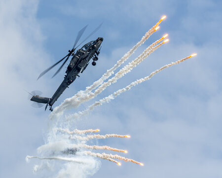 Aerial view of an Apache AH64D military helicopter maneuvers against a bright blue sky, leaving trails of smoke and flares, Changi, Singapore.