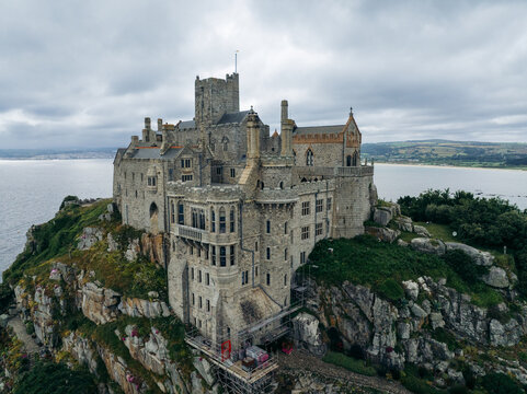 Aerial view of St Michael's Mount, a tidal island crowned by a medieval castle, rises majestically from the sea, its grey stone contrasting with the cloudy sky, Marazion, England, United Kingdom.