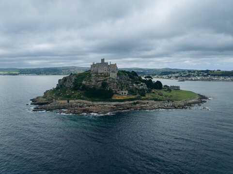 Aerial view of St Michael's Mount rising majestically from the sea, its ancient stone walls a stark contrast to the dark, swirling waters below, Marazion, England, United Kingdom.