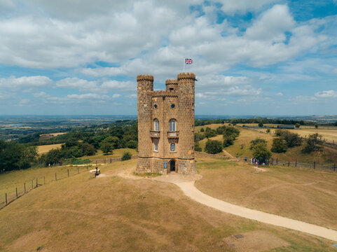 Aerial view of Broadway Tower standing tall against the horizon, its honey-colored stone contrasting with the surrounding lush greenery, Broadway, England, United Kingdom.