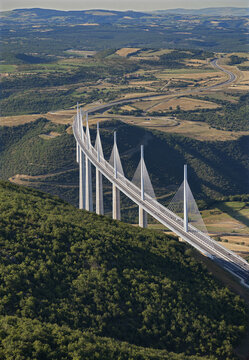 Aerial view of the Viaduc de Millau piercing the sky with its sleek white pillars, a modern marvel amidst the rolling green hills, Millau, Occitanie, France.