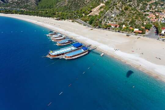 Aerial view of boats lined up along the bright sandy beach where the turquoise sea meets the shore, Oludeniz, Mugla, Turkey.