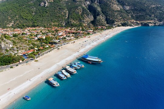 Aerial view of boats rest on the shores of the pristine beach, where azure waters meet the golden sands near Oludeniz, Mugla, Turkey.