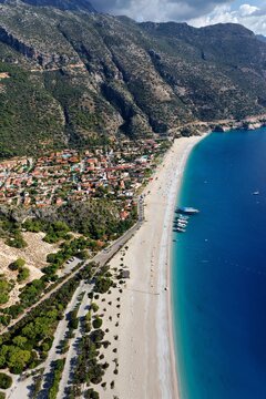 Aerial view of the stark white beach meeting the turquoise sea, nestled beside the rugged, verdant mountains of Oludeniz, Mugla, Turkey.