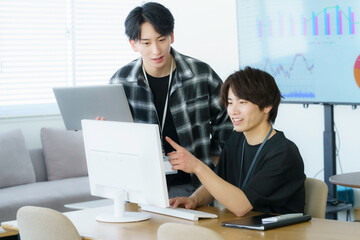Obraz premium オフィスでパソコン作業をするカジュアルな服装の若い日本人男性2人